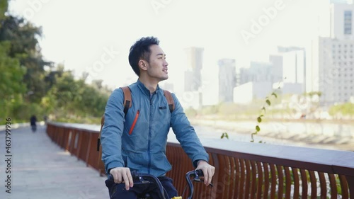 young asian man riding bicycle on riverfront path looking at view photo