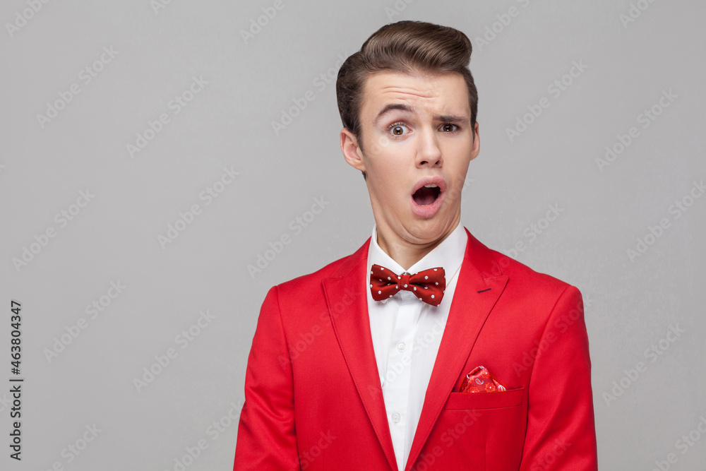 Portrait of funny surprised man with stylish hairdo in red tuxedo and bow tie staring in surprise at camera with comical dumb grimace, making a face. indoor studio shot isolated on gray background Portrait of funny surprised man with stylish hairdo in red tuxedo and bow tie staring in surprise at camera with comical dumb grimace, making a face. indoor studio shot isolated on gray background