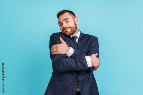 Fotografía I love myself! Portrait of narcissistic selfish young adult man in suit embracing herself, closed eyes and smiling with pleasure, complacency and egoism