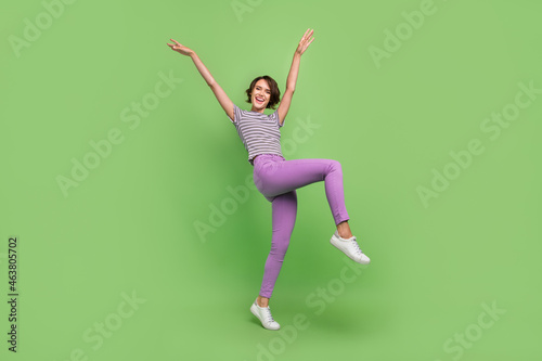 Photo of cute charming young woman dressed striped t-shirt smiling walking rising arms isolated green color background
