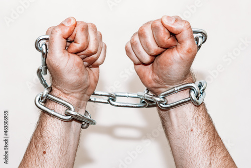 Men's hand in a steel chain.Steel chains in the hands of man on a gray wall background.Toned.Closeup,selective focus.