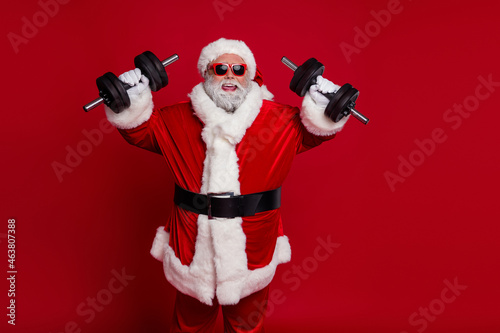 Photo of fat slimming santa claus wear red headwear hat dark glasses smiling holding dumbbells isolated red color background