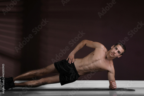 Handsome man doing side plank exercise on floor indoors
