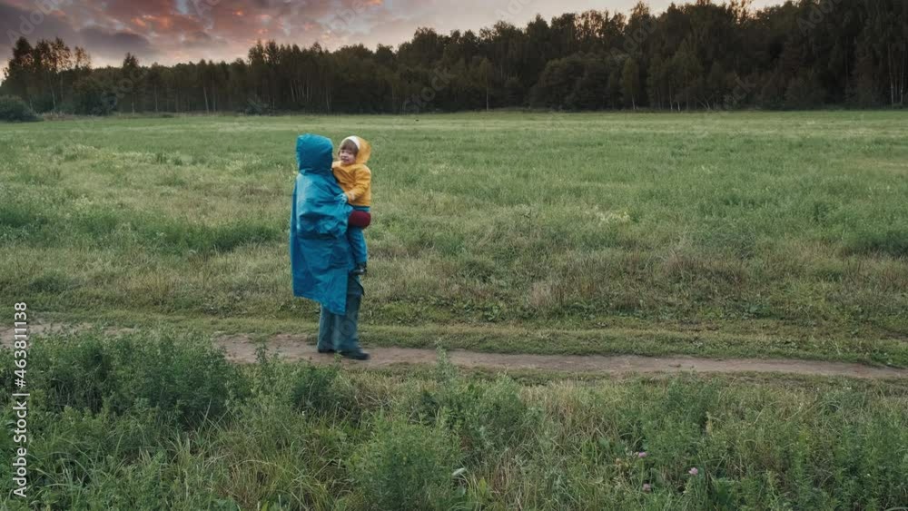 Woman walks in the park in the evening with a small child. People in raincoats, cloudy weather. The concept of outdoor walks and atmospheric phenomena Woman walks in the park in the evening with a small child. People in raincoats, cloudy weather. The concept of outdoor walks and atmospheric phenomena