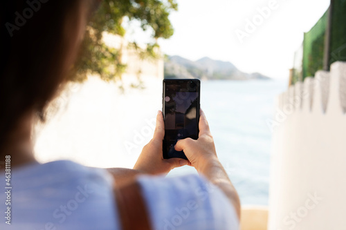 Young woman taking photo with phone near the sea. Happy woman enjoy in sunny day.