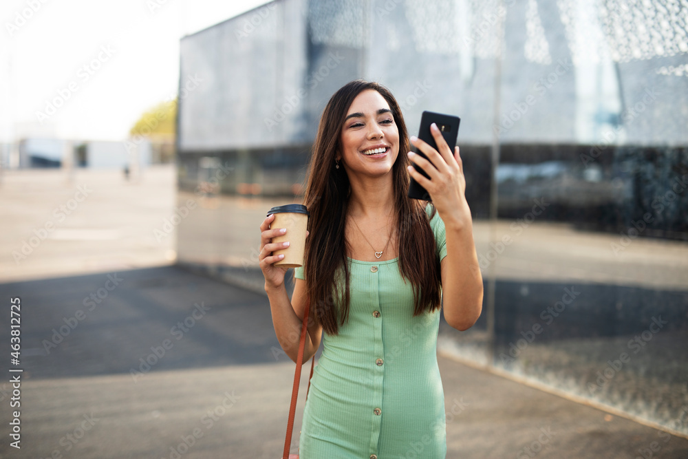  Young girl with coffee to go holding smartphone. Beautiful woman using the phone while enjoying in fresh coffee.