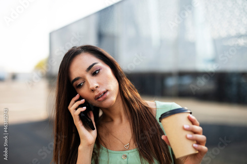 Young girl with coffee to go holding smartphone. Beautiful woman talking to the phone while enjoying in fresh coffee