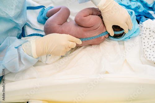 Medical examination of the newborn in the first few minutes of life. Newborn baby after delivery in labor room. Doctor and midwife measure height newborn boy after birth in hospital.