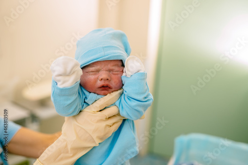 Schilderij op canvas The doctor hands in glaves holding the just born baby boy dressed in clothes for newborns in hospital
