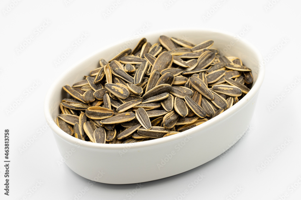 Sunflower seeds on a white background. Ceramic plate filled with sunflower seeds