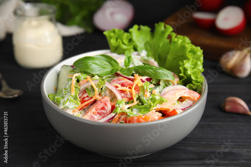 Bowl of delicious vegetable salad dressed with mayonnaise on black wooden table, closeup