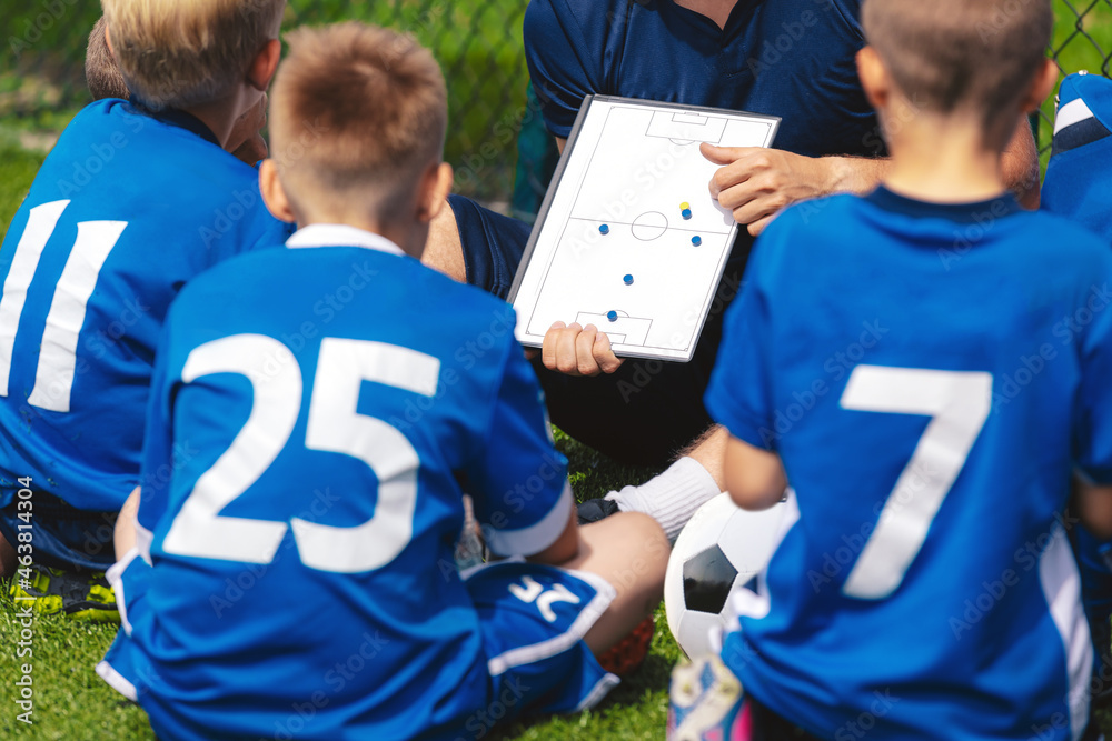 Fototapeta premium Anonymous football coach teaching kids on grass field. Coach explains a game strategy using white board. Coach coaching boys. Soccer football training session for children. Football tactic education