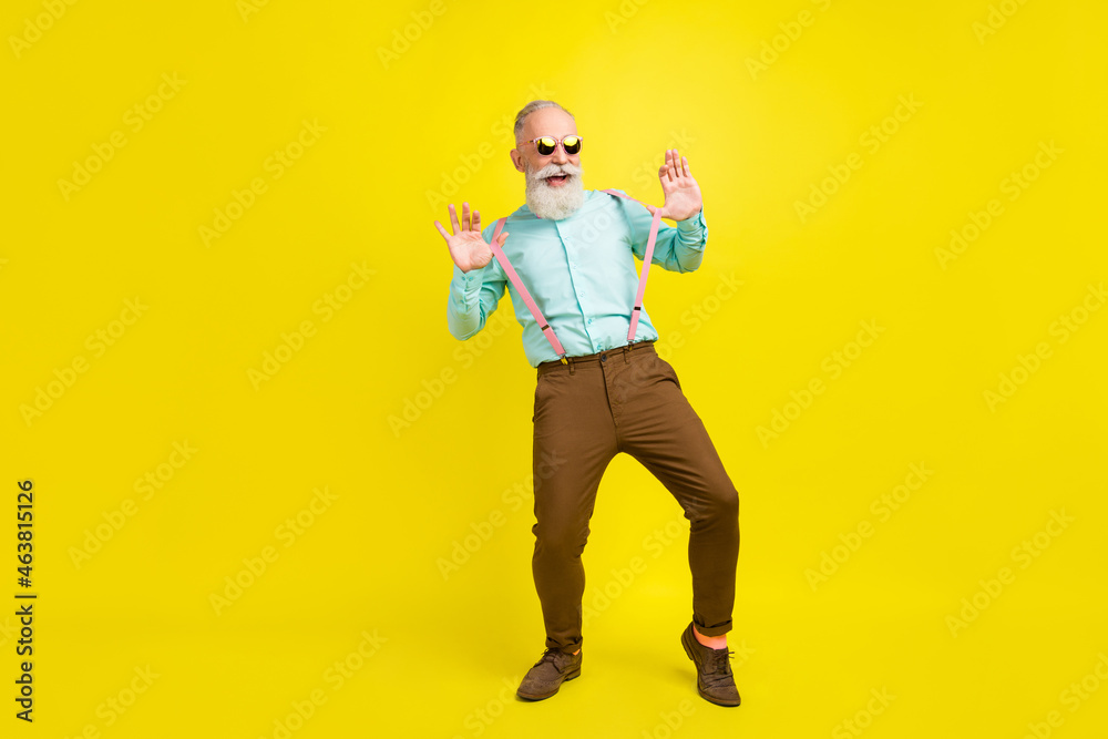 Full length body size photo elder man wearing suspenders sunglass relaxing on holidays laughing isolated bright yellow color background Full length body size photo elder man wearing suspenders sunglass relaxing on holidays laughing isolated bright yellow color background