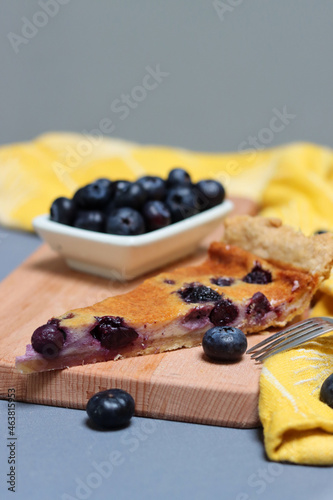 Slice of Blueberry tart on wooden cutting board. Sweet blueberry cake on a table. Homemade dessert close up photo. Healthy eating concept. Grey background with copy space. 