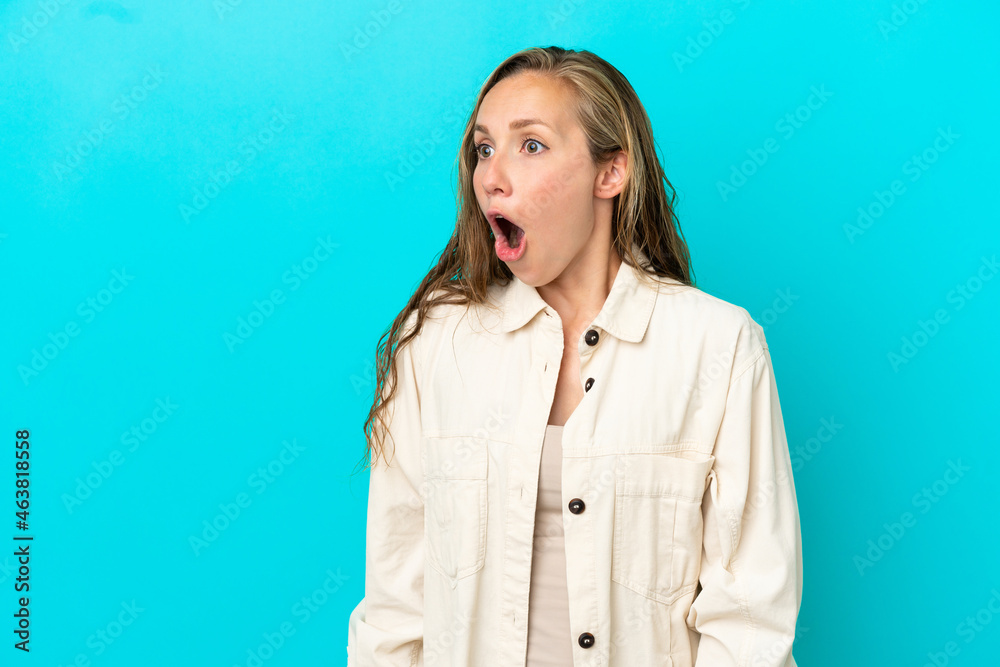 Young caucasian woman isolated on blue background doing surprise gesture while looking to the side Young caucasian woman isolated on blue background doing surprise gesture while looking to the side