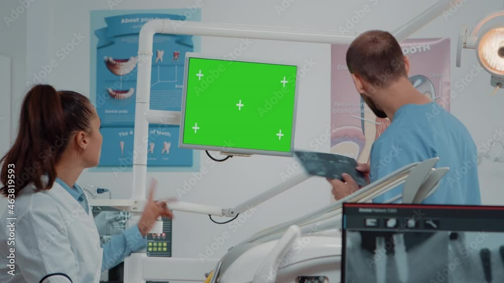 Dental team working with green screen on computer in cabinet for oral care. Dentist and assistant talking while looking at isolated background and mockup template for dentistry. Dental team working with green screen on computer in cabinet for oral care. Dentist and assistant talking while looking at isolated background and mockup template for dentistry.