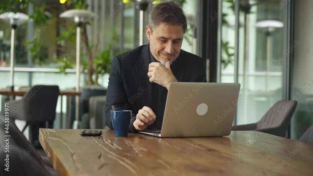 Business portrait - businessman sitting in in office working with laptop computer, thinking. Mature age, middle age, mid adult man in 50s with happy confident smile. Copy space. Business portrait - businessman sitting in in office working with laptop computer, thinking. Mature age, middle age, mid adult man in 50s with happy confident smile. Copy space.