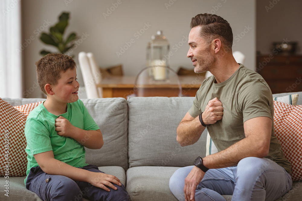 Caucasian father and son communicating using sign language while sitting on the couch at home Caucasian father and son communicating using sign language while sitting on the couch at home