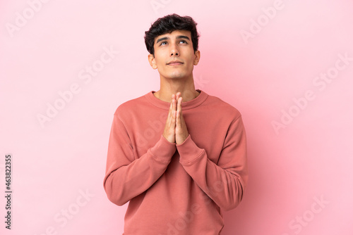 Young Argentinian man isolated on pink background keeps palm together. Person asks for something