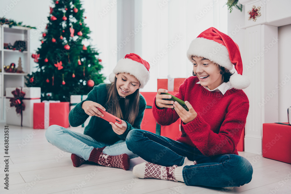 Photo of two gamer kids hold phone enjoy x-mas video game event wear jumper hat in decorated home indoors Photo of two gamer kids hold phone enjoy x-mas video game event wear jumper hat in decorated home indoors