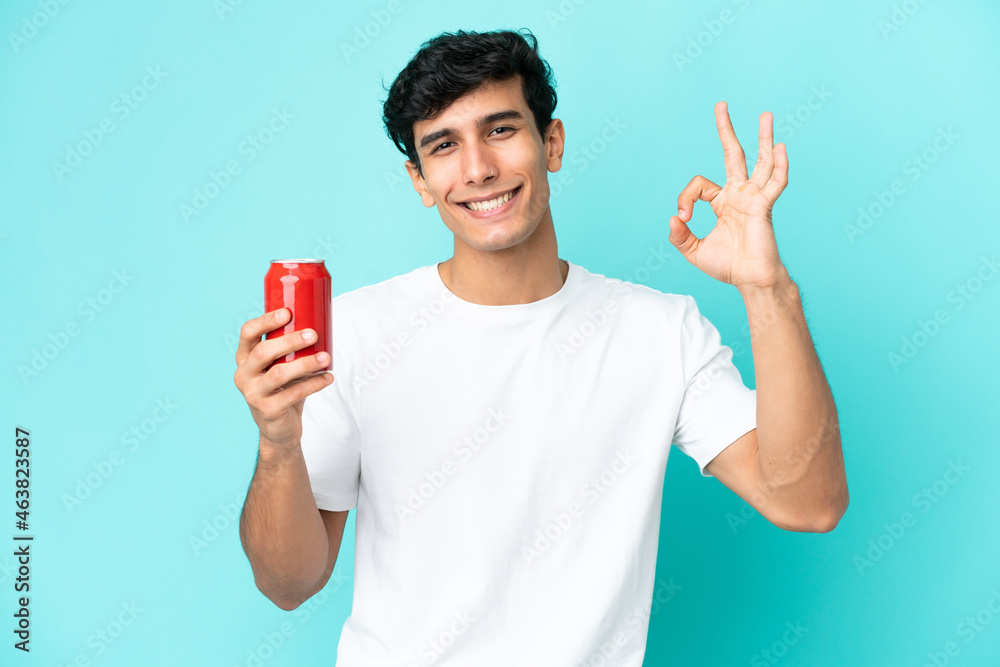 Young Argentinian man holding a refreshment isolated on blue background showing ok sign with fingers