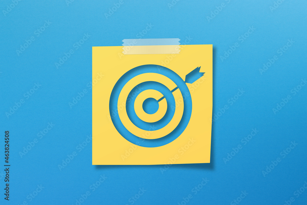 Yellow sticky note paper with target sign on blue background Yellow sticky note paper with target sign on blue background
