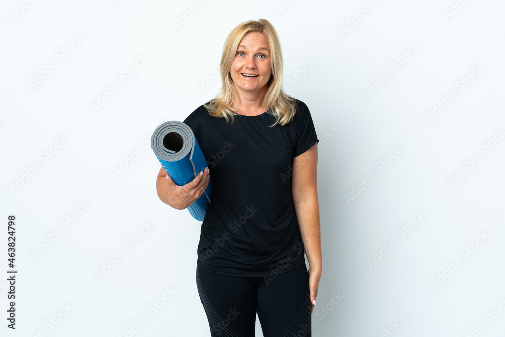 Middle age woman going to yoga classes while holding a mat isolated on white background with surprise and shocked facial expression Middle age woman going to yoga classes while holding a mat isolated on white background with surprise and shocked facial expression