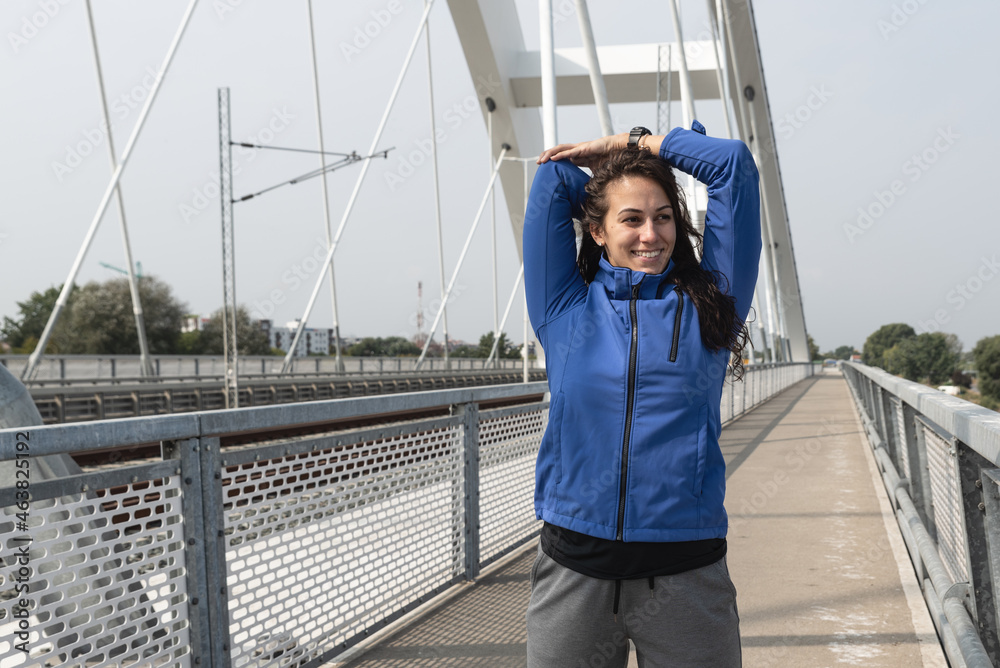 Obraz premium Young beautiful happy sporty fitness woman standing on the bridge stretching her muscles preparing for jogging and running exercise while she concentrate for workout and training marathon motivation