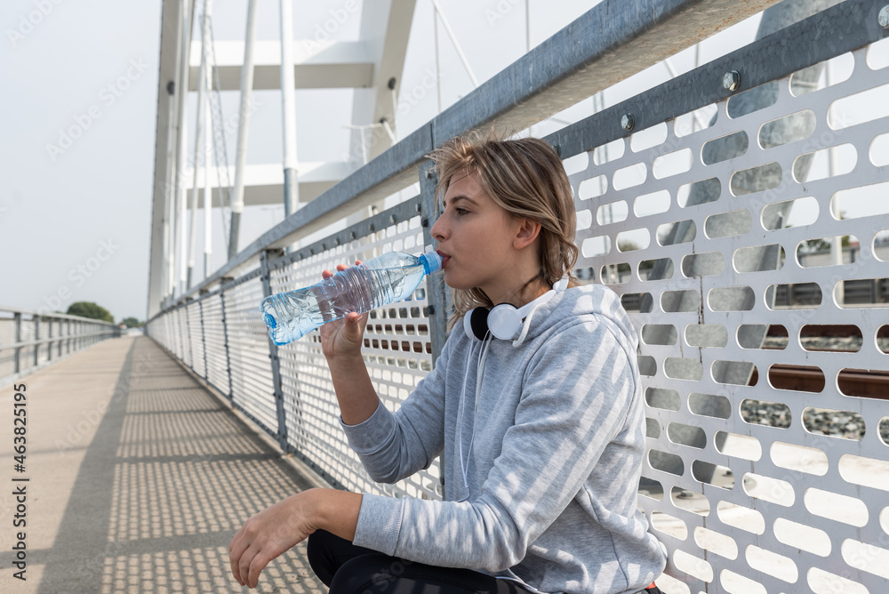 Young happy self loved sporty fitness runner woman standing and taking a break with bottle of water after hard running and jogging exercise for healthy life and clear mind preparing for marathon