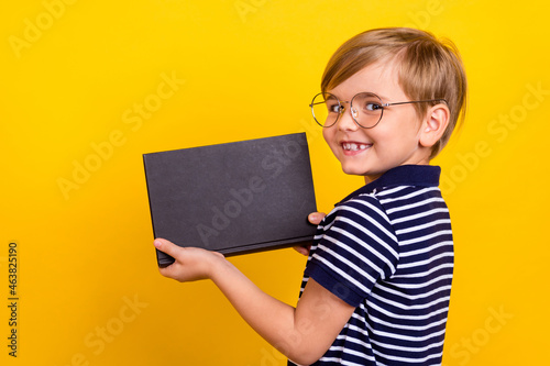 Photo portrait little boy wearing striped t-shirt glasses keeping book smiling isolated vibrant yellow color background