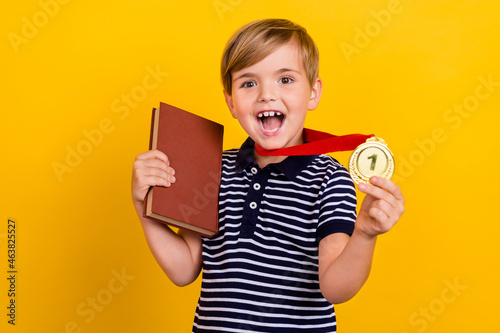 Photo portrait little boy wearing golden medal prize smartest student keeping book isolated vibrant yellow color background photo
