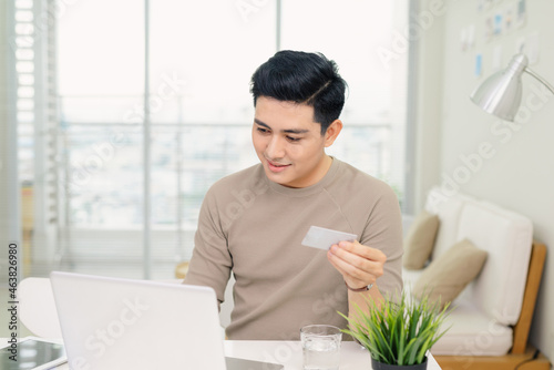  handsome young businessman using a computer while holding a credit card in an home office