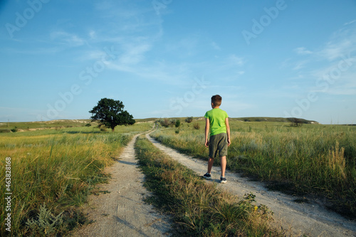 Boy walk among filds and hills and looking something by the hand and points to the sky into the distance, standing on the big road