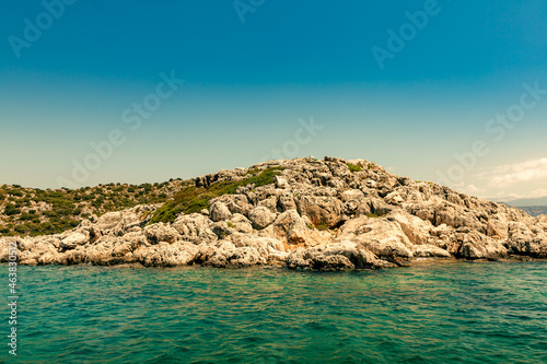 Rocky cape with green vegetation against the background of turquoise sea water. Sea horizon. Free space