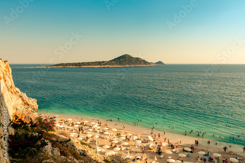 Turquoise blue waters of a lagoon in the Mediterranean Sea overlooking Kaputas Beach at the bottom of a deep gorge and a mountain island in the background photo