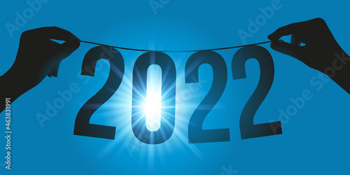 Carte de vœux présentant l’espoir et l’avenir pour l’année 2022 avec une guirlande sur tenue par deux mains, face aux rayons du soleil.