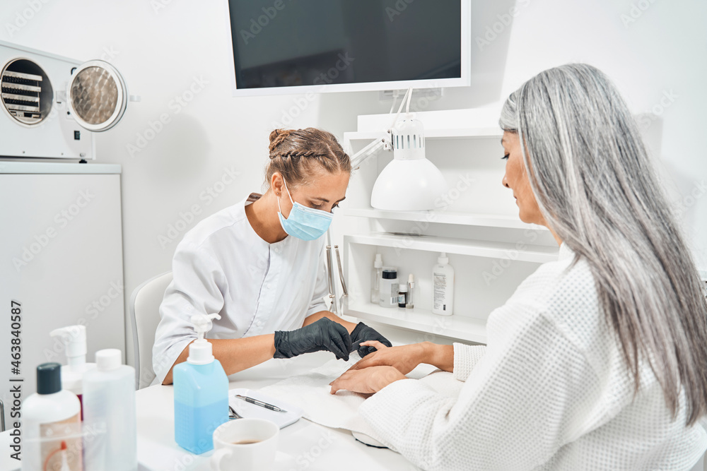 Fototapeta premium Concentrated nail master making good manicure to her client