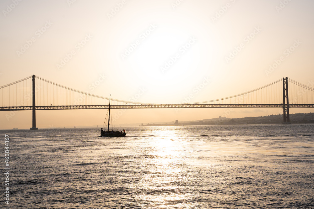 Sailing boat floating next to a bridge during sunset in Lisbon