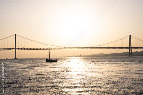 Sailing boat floating next to a bridge during sunset in Lisbon
