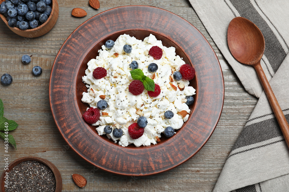 Fresh cottage cheese with berries and mint in plate on wooden table, flat lay