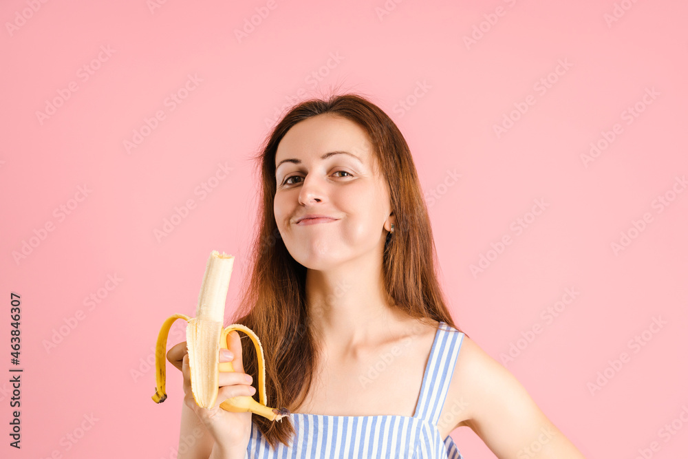 A hungry woman with an appetite is eating a delicious ripe banana on a pink background A hungry woman with an appetite is eating a delicious ripe banana on a pink background
