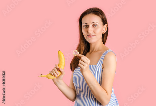 A woman shows how to put a condom on a banana. Studio shot on a pink background. The concept of sex education