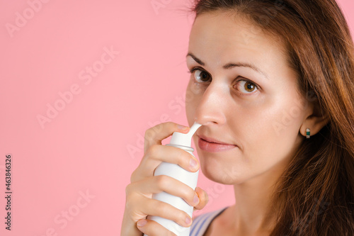 A sick woman uses a spray with sea water on a pink background