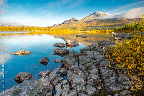 Mountain and sky reflecting in lake in early morning of autumn. Autumn colors in remote arctic landscape. Nieras mountain reflects in Lulealven dam in Stora Sjofallet national park, Sweden. photo