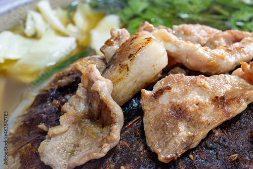A preparation of roasted meat with sauce of vegetable on Hot Pot - Mu Kratha, close up..Grilled slice pork at Thai Barbecue style, macro view. photo