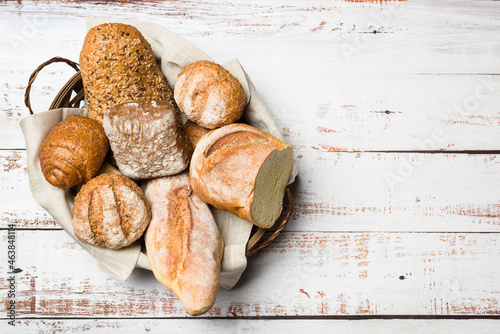 Fotografi Assortment of baked bread into basket on wooden table. Top view