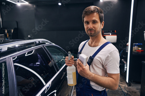 Worker of repair shop posing with cleaning liquid and sponge