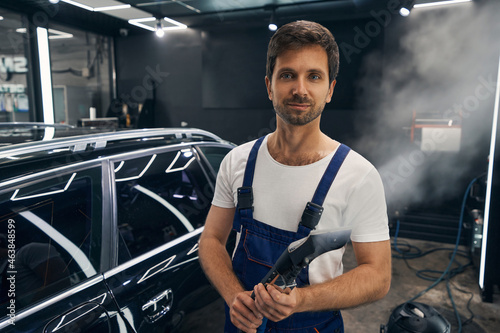 Pleased car technician standing with turned-on steam cleaner