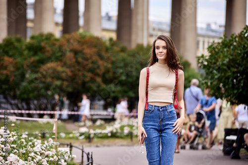 Slender woman 18 years old stands outdoors near fountain.