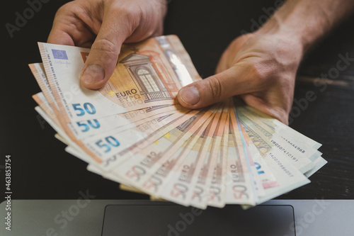 business man counting money. rich male hands holds and count cash banknotes of 50 euros bills or notes currency in front of a laptop